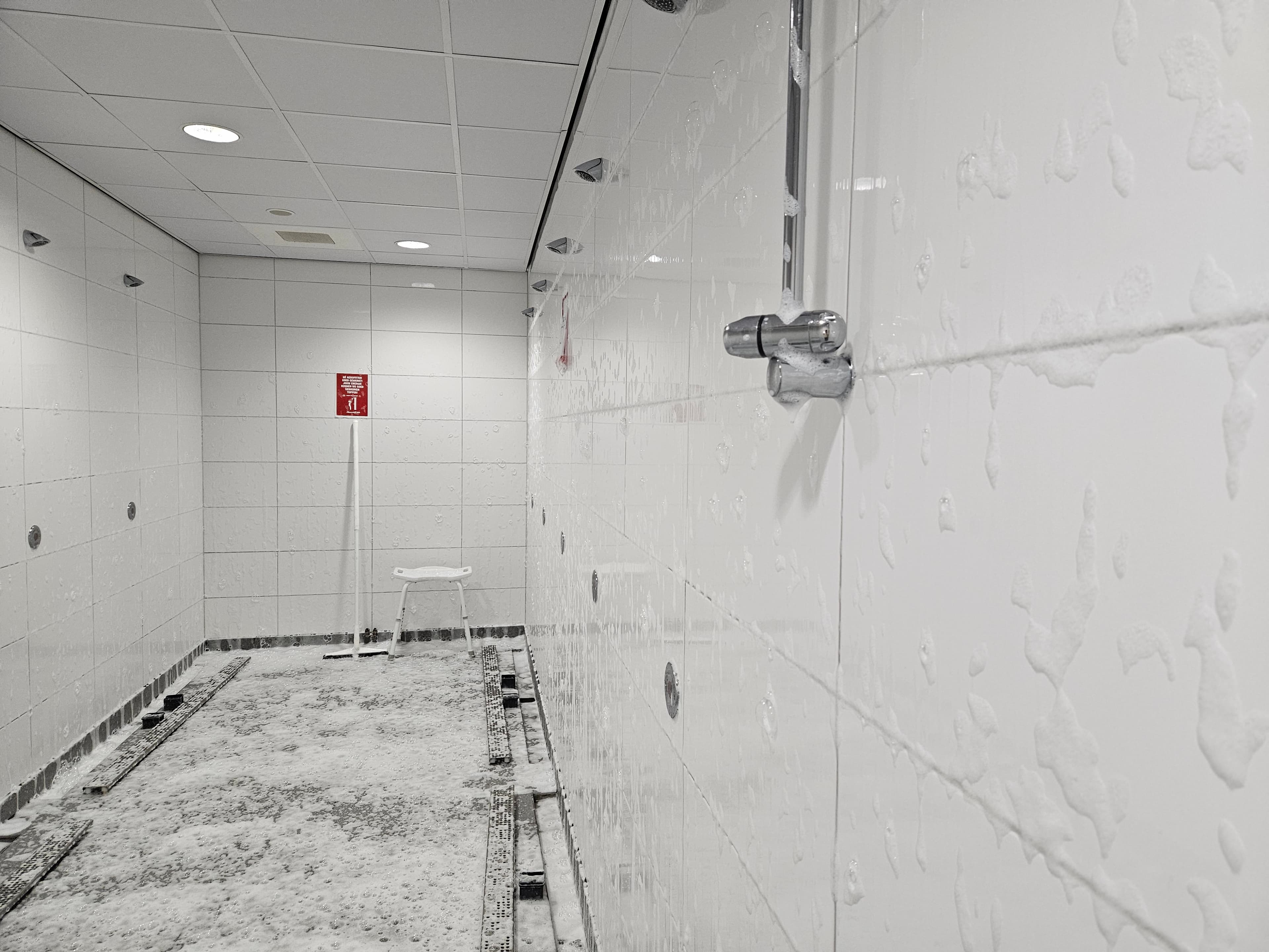 White tiled public shower room with walls and floor covered in thick soap suds.